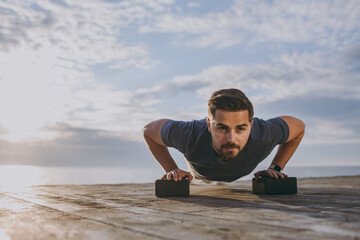 Fototapeta na wymiar Full body front view young strong fit sportsman man in sports clothes shorts warm up train do push-ups exercises on floor at sunrise sun over sea beach outdoor on pier seaside in summer day morning