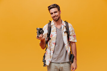 Joyful bearded guy in grey t-shirt and fashionable printed shirt smiling and holding camera on...