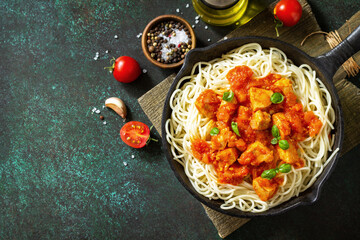 Healthy food, Italian pasta. Spaghetti with chicken and vegetables in tomato sauce in a cast iron skillet on a stone countertop. Top view flat lay background. Copy space.