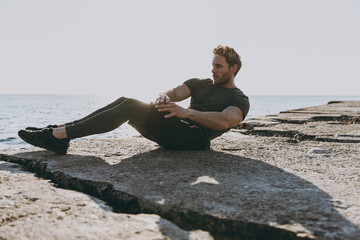 Full size profile young strong sporty toned athletic fit sportsman man 20s wear sports clothes warm up training do abs exercises at sunrise sun over sea beach outdoor seaside in summer day morning