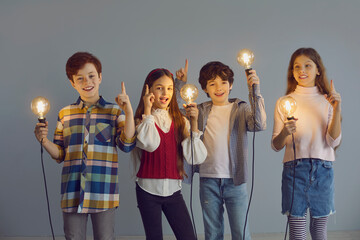 Team of kids with lightbulbs in studio. Intelligent little children holding light bulbs index...