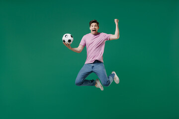 Fototapeta na wymiar Full size body length young fun man fan wear pink t-shirt cheer up support football sport team hold in hand soccer ball watch tv live stream scream jump isolated on dark green color background studio.