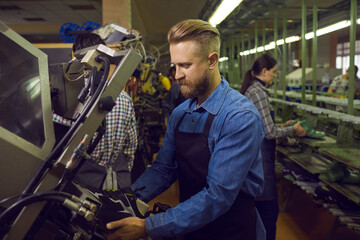 Side view of serious focused male shoe factory worker working with special industrial machinery...