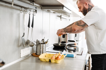 Mid aged white bearded man cooking fried eggs