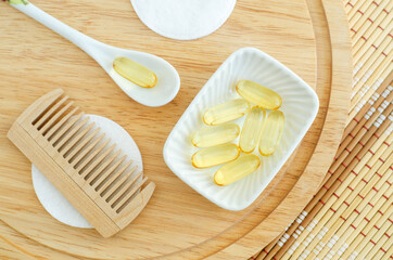 Small white bowl with cosmetic oil (face serum, cod fish oil) capsules, cotton pads and wooden hair...