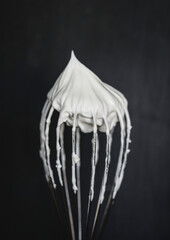 Close up of a wire whisk with whipped cream on top