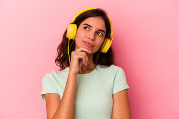 Young caucasian woman listening music isolated on pink background looking sideways with doubtful and skeptical expression.