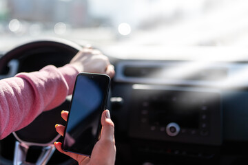 Hand holds the cell phone against the background of the steering wheel of the car.