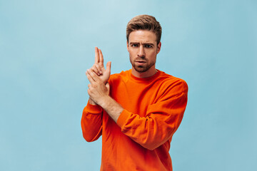 Serious bearded man with cool hairstyle in fashionable bright orange clothes looking into camera...