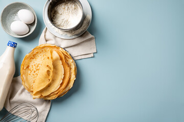 Stack of homemade crepes and ingredients for making thin pancakes around on blue background. Top...