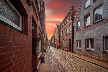 Fototapeta na wymiar Narrow street in a northern German old town with brick houses under a red evening sky, edited photo