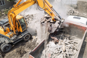 Excavator loads construction debris of old building after destruction in dump truck, aerial view...