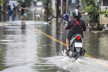 An unidentified woman riding a scooter through a flooded street.