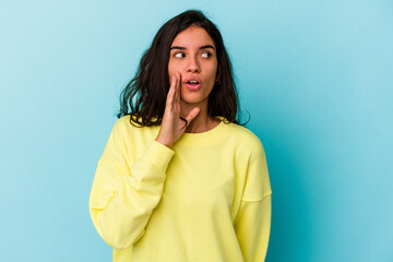 Young caucasian woman isolated on blue background is saying a secret hot braking news and looking aside