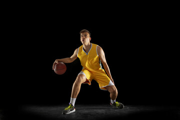 Fototapeta na wymiar Basketball player with a ball in action and motion isolated on dark black studio background. Advertising concept. Strong Caucasian athlete practicing with basketball ball.