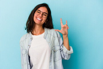 Young caucasian woman isolated on blue background showing a horns gesture as a revolution concept.