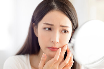 Young woman looking at  mirror and checking the  acne problem at home