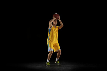 Fototapeta na wymiar Three-point shot. Basketball player with a ball training isolated on dark black studio background. Advertising concept. Sport, motion, activity and movement concepts.