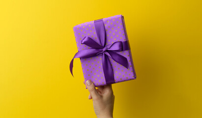 female hand are holding a purole gift box on a yellow background