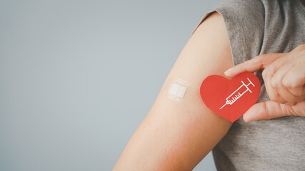 senior woman holding red heart shape with  syringe and showing her arm with bandage after got vaccinated or inoculation due to spread of corona virus, population, social or herd immunity concept - obrazy, fototapety, plakaty