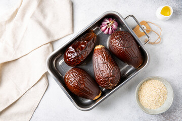 Whole oven-baked eggplant and garlic in metal baking dish on concrete background.