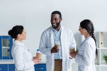 Fototapeta premium Happy multiethnic doctors holding paper cups in clinic