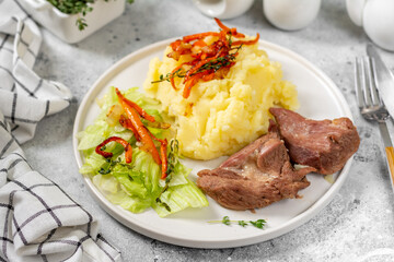 Mashed potatoes with baked turkey meat in a white plate on a light gray kitchen table closeup