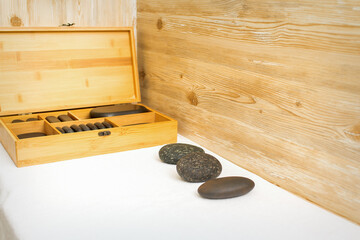 Black massage stones lying near the wooden box with massage rocks on the towel on the table