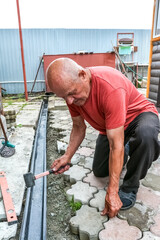 An elderly man makes a pedestrian path out of paving slabs. Labor activity on the household plot....