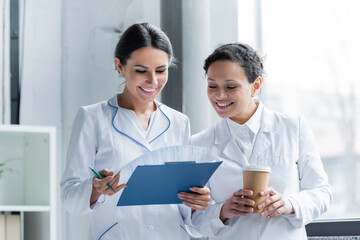 Multiethnic doctors with coffee and clipboard smiling in hospital