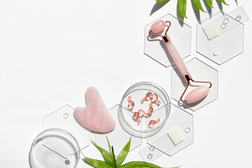 Pink quarts face roller, gua sha stone, serum capsules in chemical glass dish, hexagons, palm...