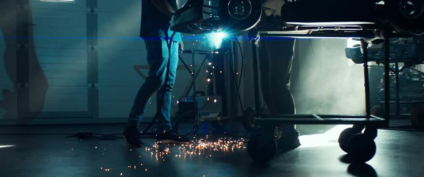 CU Sparks falling on the ground as mechanic welding a go kart car inside garage. 100 FPS slow motion. Shot with 2x anamorphic lens