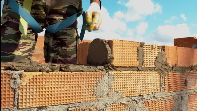 Construction of a brick wall of a residential multi-storey building. A builder carefully lays bricks on top of each other. Construction site, work. High quality. 4k footage.