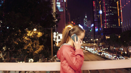 Young woman goes in the city and talk by the phone and shows on building at night, Hong Kong.
