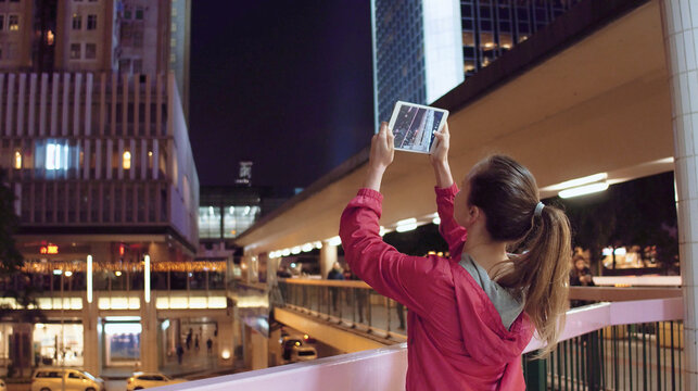 Young woman taking photos of buildings on her tablet pc at night, Hong Kong.