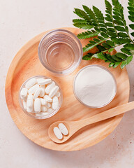 Collagen powder, pills and glass of water on wooden tray, top view