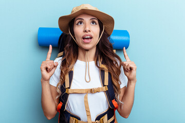 Young hiker mixed race woman isolated on blue background pointing upside with opened mouth.