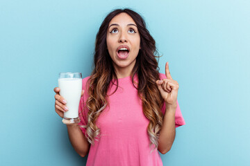 Young mixed race woman holding a glass of milk isolated on blue background pointing upside with opened mouth.