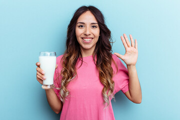 Young mixed race woman holding a glass of milk isolated on blue background smiling cheerful showing number five with fingers.