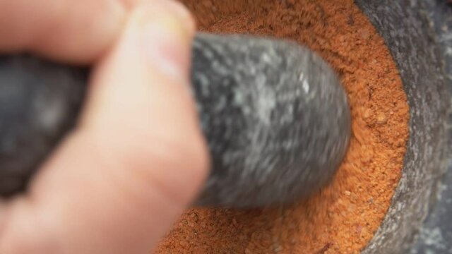 Super close-up of heavy pestle grinding and mixing spices in a grey stone mortar
