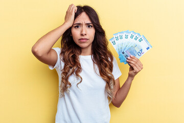 Young mixed race woman holding bills isolated on yellow background being shocked, she has remembered important meeting.