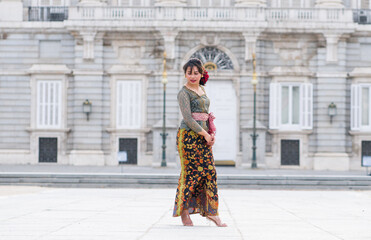 young happy Indonesian woman from Bali having vacation in Europe - beautiful and exotic Balinese tourist girl dancing in traditional outfit touring in the city enjoying holidays