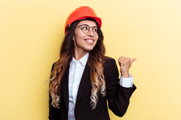 Young architect mixed race woman isolated on yellow background points with thumb finger away, laughing and carefree.