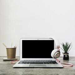 Fototapeta premium Laptop with blank black screen, flower, office supplies and headphones hang over the monitor. Home interior or office background. Copy space.