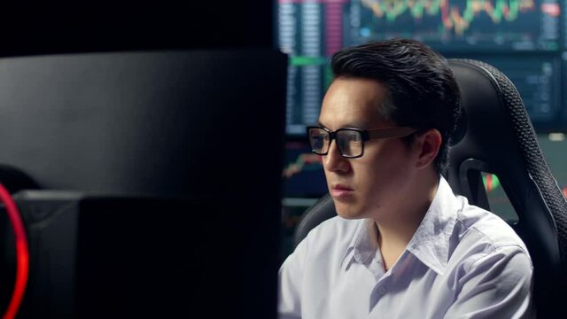 Asian Male Stock Market Broker Working On Computer With Analyzing Graphs On Multiple Computer Screens At Background

