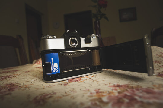An old analog camera is on the table in the house. The camera is open to the back so you can see the photographic film.