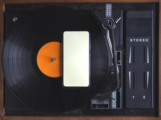 The top view of the new modern smartphone is on the music record on the turntable. The phone has a...