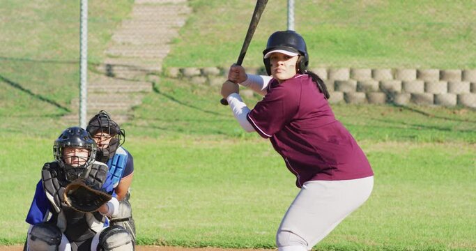 Diverse group of female baseball players playing on the field, hitter swinging for pitched ball