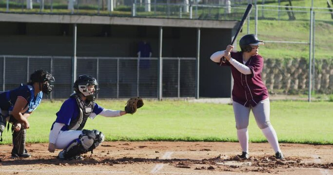 Diverse group of female baseball players playing on the field, hitter hitting pitched ball