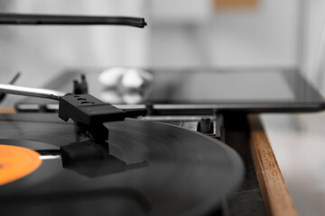 Obraz na płótnie Canvas Selective focus on the head of a gramophone moving on a music record. behind it is a tablet computer and white wireless headphones on it.
